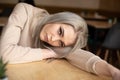 Portrait of young gorgeous thoughtful woman with long grey hair with make-up laying head on hand on table in cafe. Royalty Free Stock Photo