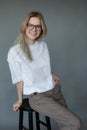 Portrait of young gorgeous woman sitting on black stool, leaning on hand, posing on grey background. Studio, vertical. Royalty Free Stock Photo