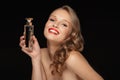 Portrait of young gorgeous woman with wavy hair and red lips holding perfume in hand while joyfully looking in camera