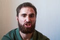 Portrait of young guy with dark beard with various emotions on his face in green shirt.