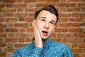 Portrait young guy dressed blue shirt. man open his eyes wide with hands, fingers and mouth. Man on brick wall background Royalty Free Stock Photo