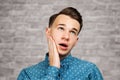 Portrait young guy dressed blue shirt. man open his eyes wide with hands, fingers and mouth. Man on brick wall background Royalty Free Stock Photo