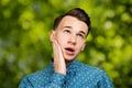 Portrait young guy dressed blue shirt. man open his eyes wide with hands, fingers and mouth. Man on green bokeh background Royalty Free Stock Photo