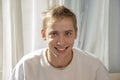 Portrait of a young guy 20-25 years old, sitting by the window and smiling. Concept: good news, good mood. Royalty Free Stock Photo