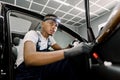 Portrait of young handsome African man worker in uniform and protective gloves performing the cleaning of car door with Royalty Free Stock Photo