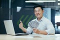 Portrait of an Asian businessman, millionaire. He sits in the office, holds money in cash, smiles Royalty Free Stock Photo