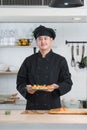 Portrait of young handsome Asian chef with black uniform and hat, holding a plate of delicious sushi, Japanese food, in restaurant Royalty Free Stock Photo