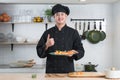 Portrait of young handsome Asian chef with black uniform and hat, holding a plate of delicious sushi, Japanese food, thumbs up Royalty Free Stock Photo