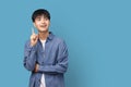Portrait of young handsome Asian man holding index finger up great Idea and looking sideways with copy space standing on blue