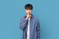 Portrait of young handsome Asian man keeping finger on his lips gesturing silent on standing blue background Royalty Free Stock Photo