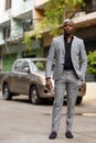 Full body shot of young handsome bald African businessman in suit outdoors Royalty Free Stock Photo