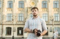 Portrait of a young handsome bearded man in striped shirt holding professional camera, shooting outdoors, stylishly dressed, Royalty Free Stock Photo