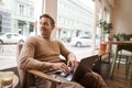 Portrait of young handsome businessman, a man with laptop, sitting in coffee shop on chair and working, freelancer doing Royalty Free Stock Photo