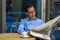 Portrait of a young handsome businessman reading a newspaper at his breakfast in coffee shop Royalty Free Stock Photo