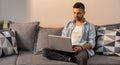 Portrait of young, handsome and busy man, working on his laptop, sitting on the sofa and wearing casual clothes. Royalty Free Stock Photo