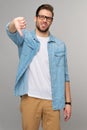 Portrait of young handsome caucasian man in jeans shirt showing big thumb down dislike gesture standing over light Royalty Free Stock Photo