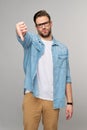 Portrait of young handsome caucasian man in jeans shirt showing big thumb down dislike gesture standing over light Royalty Free Stock Photo