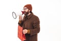 Portrait of young handsome Caucasian man screaming in the megaphone and holding red Christmas bag casual attire shades Royalty Free Stock Photo