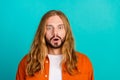 Portrait of young handsome funny man blond long hair model in orange shirt surprised speechless isolated on aquamarine Royalty Free Stock Photo