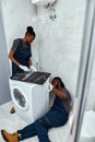 Skilled handyman troubleshooting washing machine with help of female apprentice