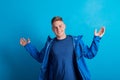 Portrait of a young man with blue anorak in a studio, standing against blue background.