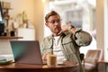 Portrait of young handsome man in glasses, businessman working in cafe, sitting with laptop, showing phone call hand Royalty Free Stock Photo