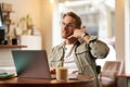 Portrait of young handsome man in glasses, businessman working in cafe, sitting with laptop, showing phone call hand Royalty Free Stock Photo