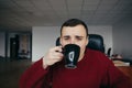 Portrait of a young handsome man sitting on workplace with cup of coffee in hand. Sleepy office worker Royalty Free Stock Photo