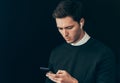 Portrait of young handsome man texting messages from his smart phone against studio black background, with wireless earphones. Royalty Free Stock Photo