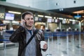 Portrait of young handsome man walking in modern airport terminal, talking smart phone, travelling with bag and coffee Royalty Free Stock Photo