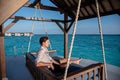 Portrait of young handsome man wearing shirt sitting on swing near water villas at the tropical beach at island luxury resort Royalty Free Stock Photo