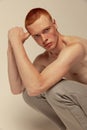 Portrait of young handsome red-haired man posing shirtless in pants isolated over grey studio background. Freckled body Royalty Free Stock Photo