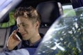 Portrait of a young handsome smiling driver sitting in his car with a smartphone in his right hand