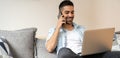 Portrait of young, handsome, smiling man talking on the phone and using his laptop while sitting on the sofa at home. Royalty Free Stock Photo