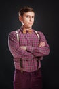 Portrait of young handsome suspicous man in vintage shirt and bow tie with hairstyle keeping hands cross while standing on black