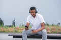 Portrait of a young and happy African American man with headphones. A man sitting on a bench and listening to music, holding a sma Royalty Free Stock Photo