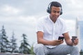 Portrait of a young and happy African American man with headphones. A man sitting on a bench and listening to music, holding a sma Royalty Free Stock Photo