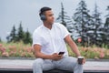 Portrait of a young and happy African American man with headphones. A man sitting on a bench and listening to music, holding a sma Royalty Free Stock Photo