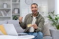 Portrait of young happy African American man sitting on couch at home in front of laptop, holding credit card and Royalty Free Stock Photo