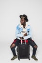 Portrait of young happy african man sitting on suitcase isolated on white background Royalty Free Stock Photo