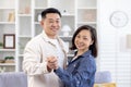 Portrait of young happy Asian couple hugging, holding hands at home dancing, man and woman looking at camera smiling Royalty Free Stock Photo