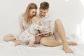 Portrait of young happy attractive family with cute cherubic infant baby toddler in white clothes sitting on white bed.