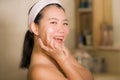 Portrait of young happy and beautiful Asian Japanese woman applying facial anti wrinkle cream and serum at bathroom mirror in skin Royalty Free Stock Photo