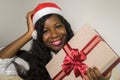 Portrait of young happy and beautiful black African American woman in Santa Claus hat holding present box smiling cheerful in Chri Royalty Free Stock Photo