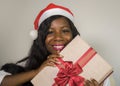 Portrait of young happy and beautiful black African American woman in Santa Claus hat holding present box smiling cheerful in Chri Royalty Free Stock Photo