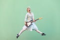 Portrait of young happy blonde woman in white shirt, skirt, and striped blouse with eyeglasses holding electric guitar, screaming Royalty Free Stock Photo