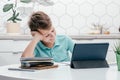 Portrait of young happy boy sitting at desk near tablet at home, leaning on hand, doing homework, having online lesson. Royalty Free Stock Photo