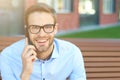 Portrait of a young happy businessman talking by phone and and smiling at camera while sitting on the bench outdoors Royalty Free Stock Photo