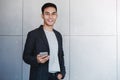 Portrait of Young Happy Businessman Using Smartphone. Standing by the Industrial Concrete Wall