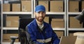 Portrait of young happy Caucasian postman in iniform and cap sitting at desk in postal office store and working at